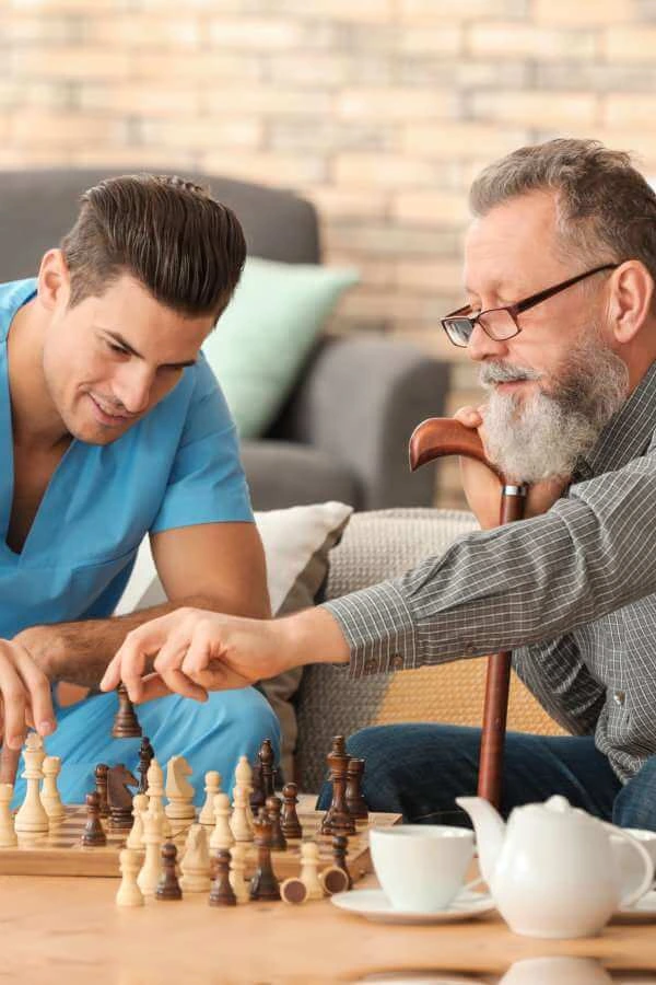 A male caregiver and an elderly man playing chess