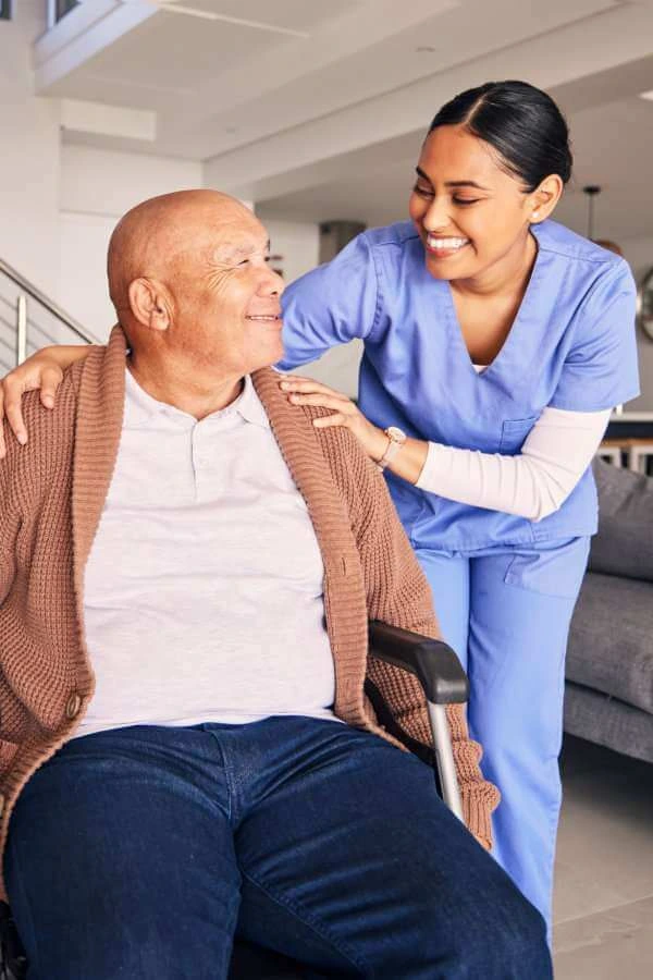 An elderly man sitting on a wheelchair and a female caregiver looking at him